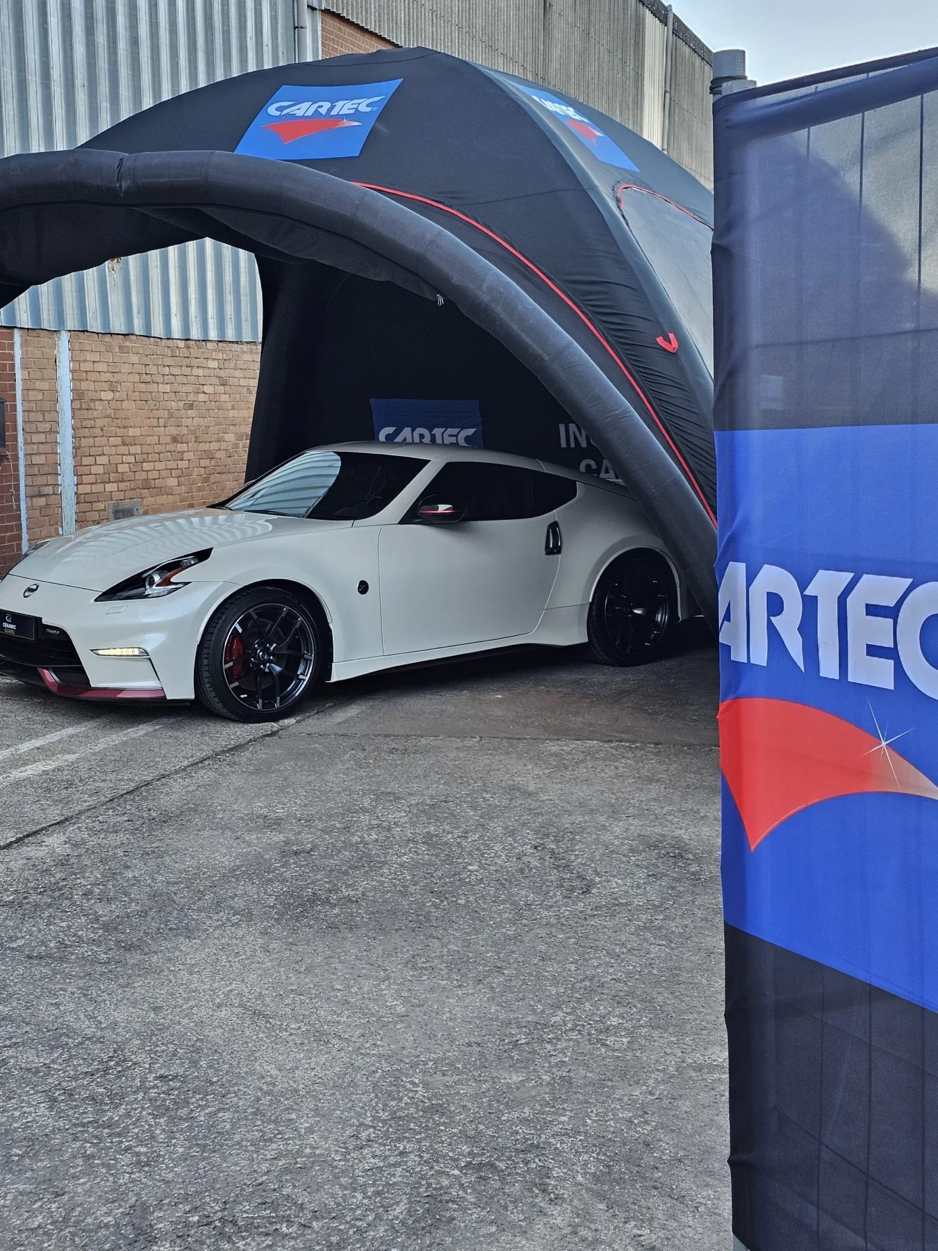 Voiture sportive blanche à côté du drapeau Cartec — démonstration gratuite Cartec du 25 avril 2026, Sébastien Cartec Wallonie