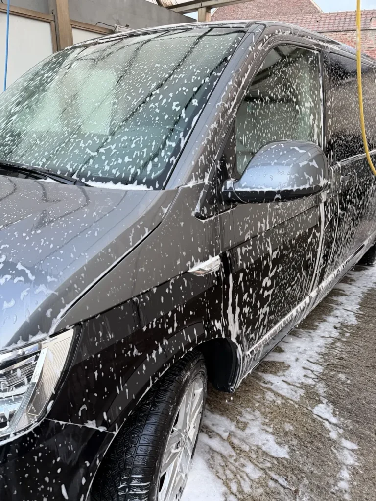 Carrosserie et pare-brise d&rsquo;un Volkswagen noir couverts de mousse lors d&rsquo;un lavage en self-wash