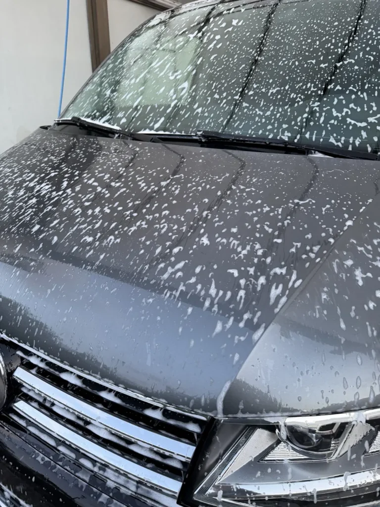 Mousse r&eacute;partie sur le capot et le pare-brise d&rsquo;un Volkswagen noir dans une station de lavage