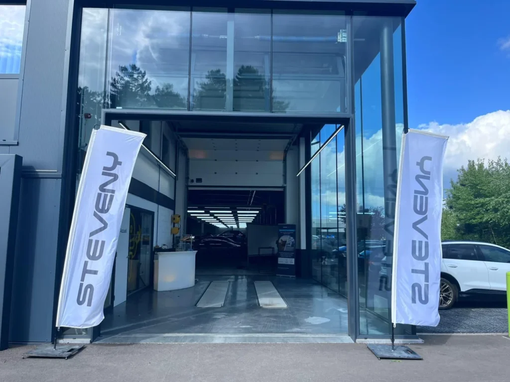 Entr&eacute;e de l&rsquo;atelier Wondercar Steveny &agrave; Namur, encadr&eacute;e par deux drapeaux Steveny